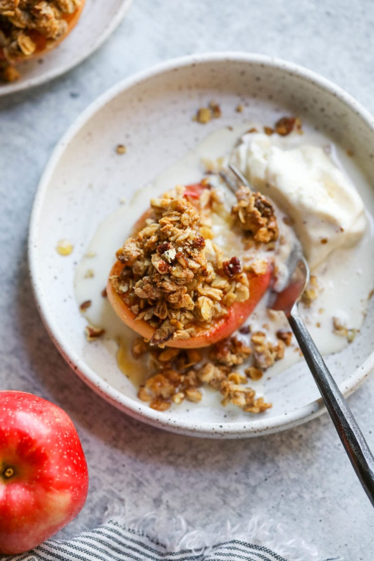 A soft baked apple half topped with oat crumble plated on a white plate