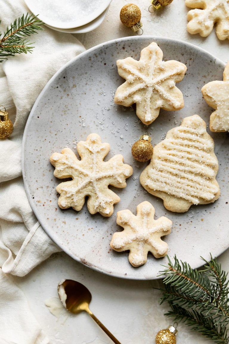 Gluten-free sugar cookies cut out in Christmas trees, snowflakes, and stars with minimal white piping on a speckled plate.