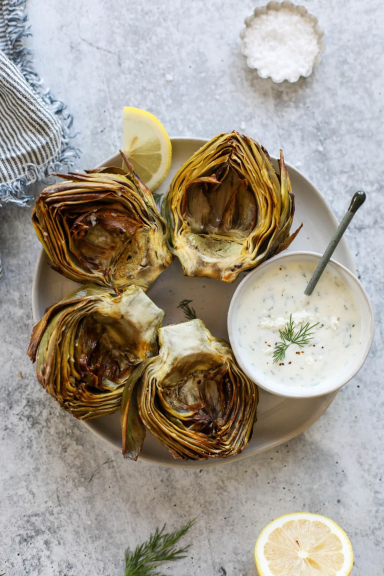 Air Fryer Artichokes on a plate with a small bowl of feta yogurt dip for dipping.