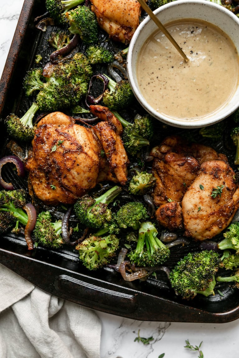 Chipotle Chicken Thighs with Broccoli on a sheet pan, a small bowl of honey mustard sauce on the side.