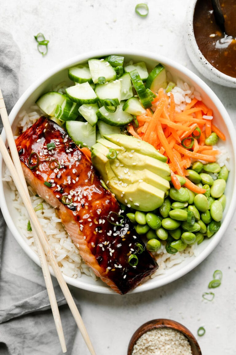 Overhead view of teriyaki salmon bowl in a white bowl with chopsticks on the edge of bowl.