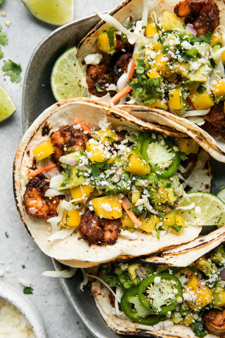 Overhead view of grilled shrimp tacos in double tortillas topped with mango avocado salsa and cojita cheese.