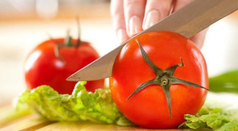 Hand using knife to cut fresh tomatoes on top of lettuce.