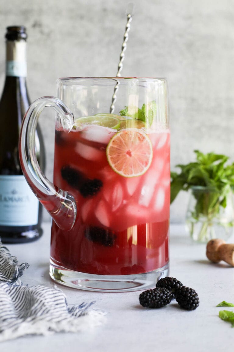 Large glass pitcher filled with blackberry lime prosecco cocktail.