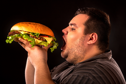 overweight person eating large hamburger