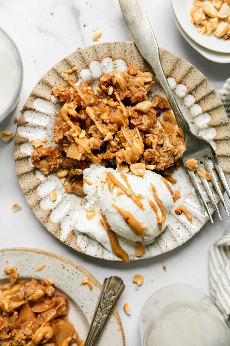 A serving of peanut butter apple crisp on scalloped edge bowl with scoop of vanilla ice cream