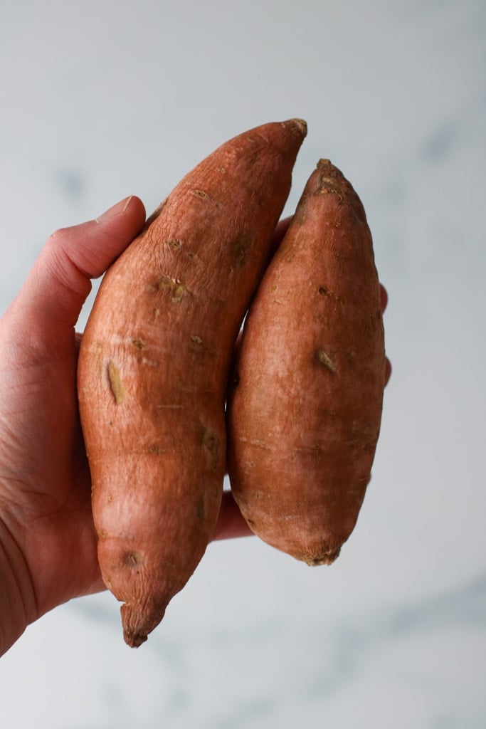 A hand holding two small sweet potatoes against marble background