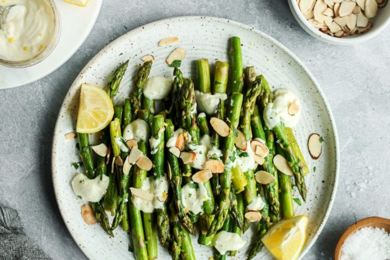 Sautéed asparagus topped with goat cheese sauce and toasted almonds on a speckled plate
