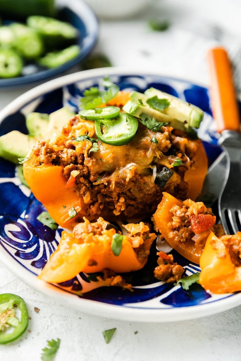 A taco stuffed bell pepper topped with cheddar cheese and jalapeño slices on blue plate.