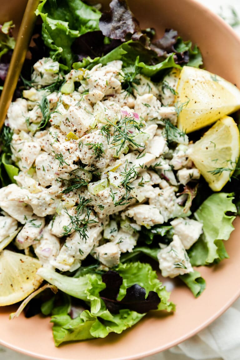 Close up view dill pickle chicken salad served over mixed greens in a pink bowl