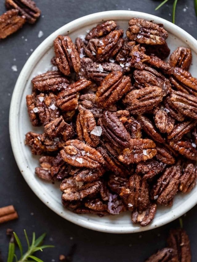 Overhead view of holiday spiced pecans on a shallow bowl sprinkled with sea salt flakes
