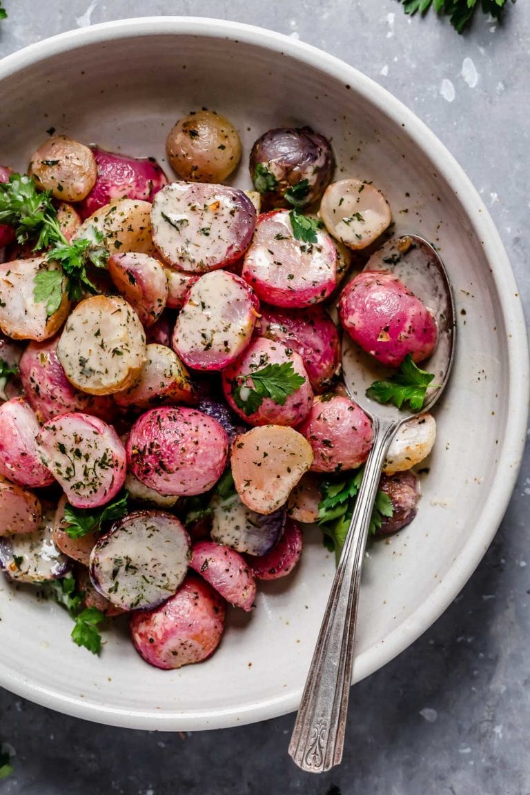 Garlic roasted radishes plated on a cream plate topped with ranch dressing and fresh herbs